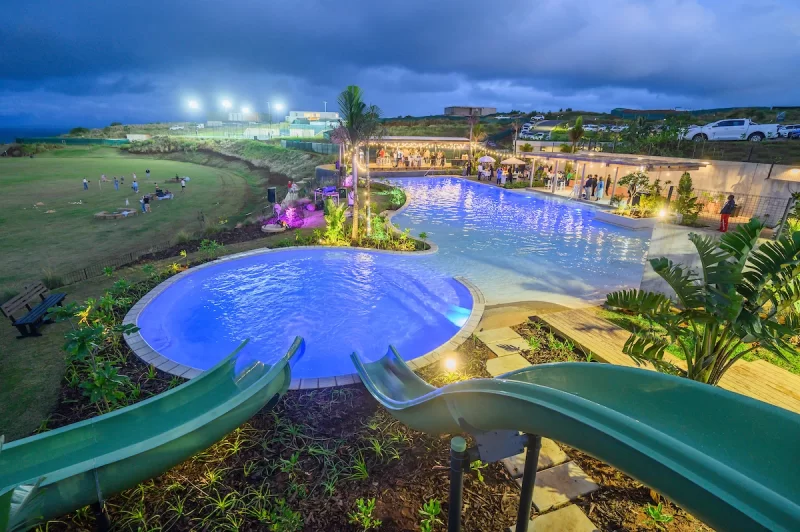 Illuminated resort pool with water slides glowing at dusk during an evening community event